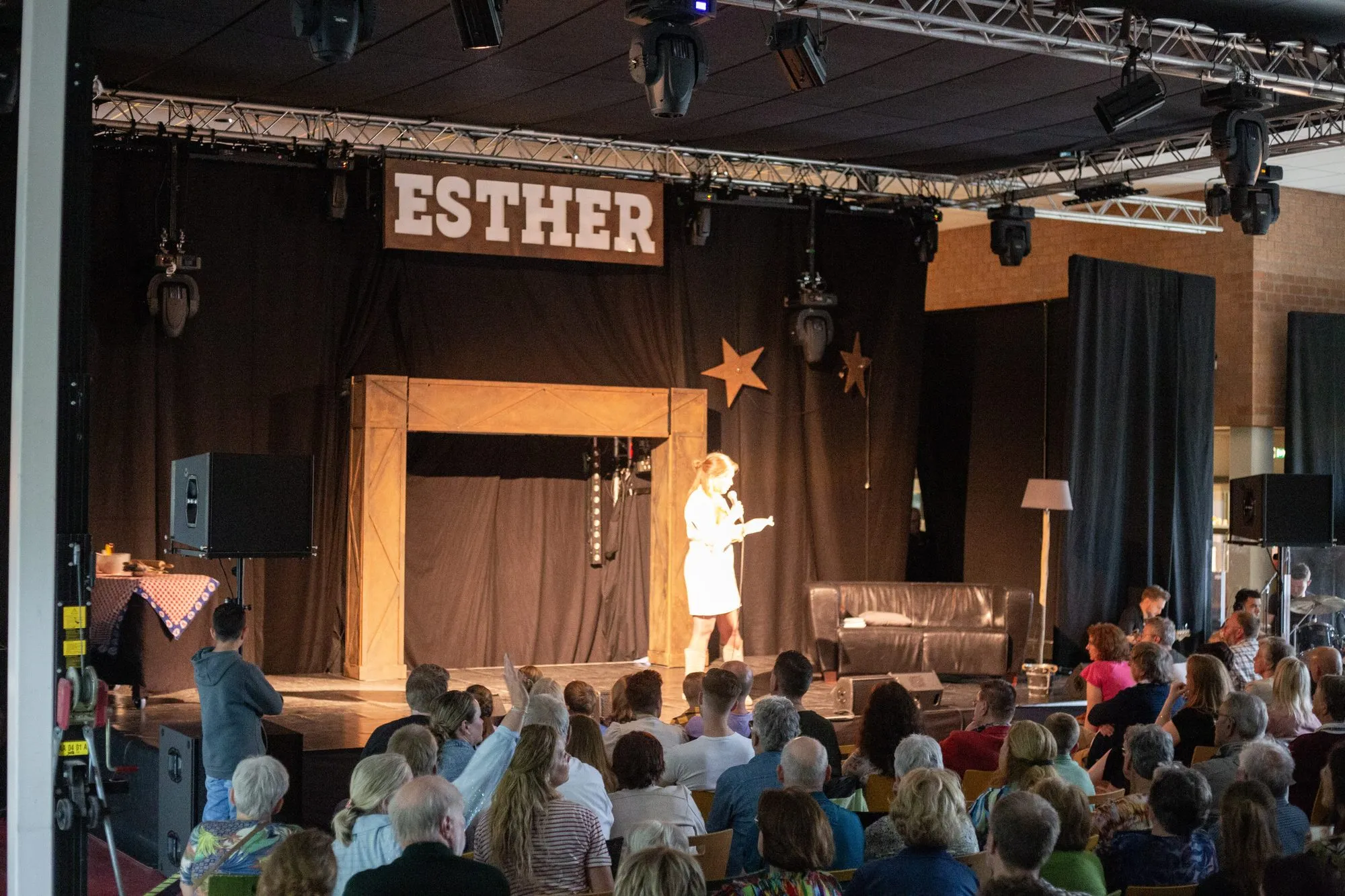 Een volle zaal kijkt naar een scène uit Esther, onder paars licht