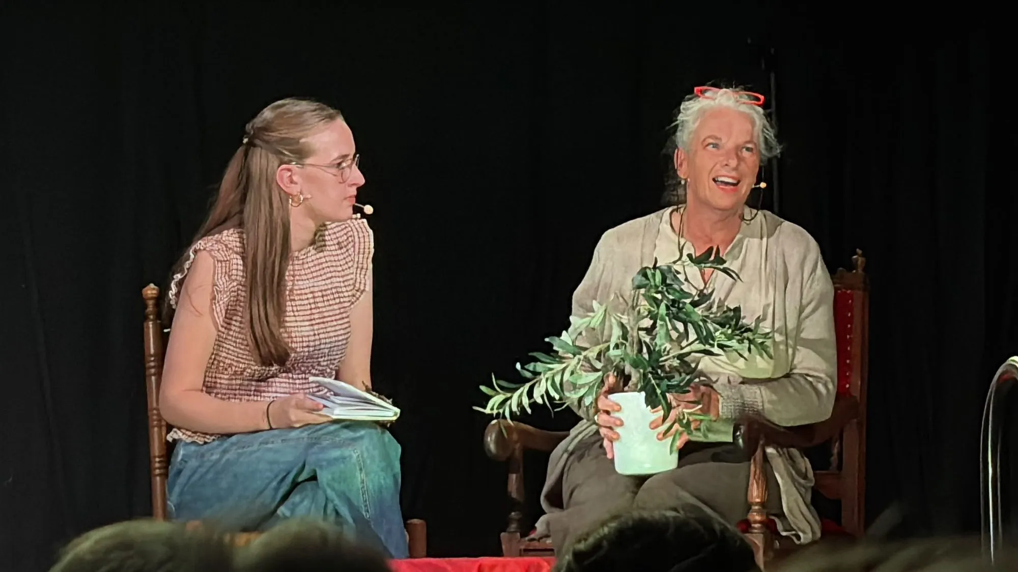 Een jonge vrouw en een oudere vrouw in gesprek, met een olijftak tussen hen in